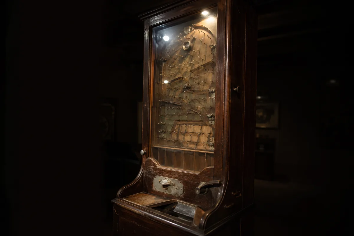 Tall antique coin-drop machine with vertical glass playfield of pins and channels